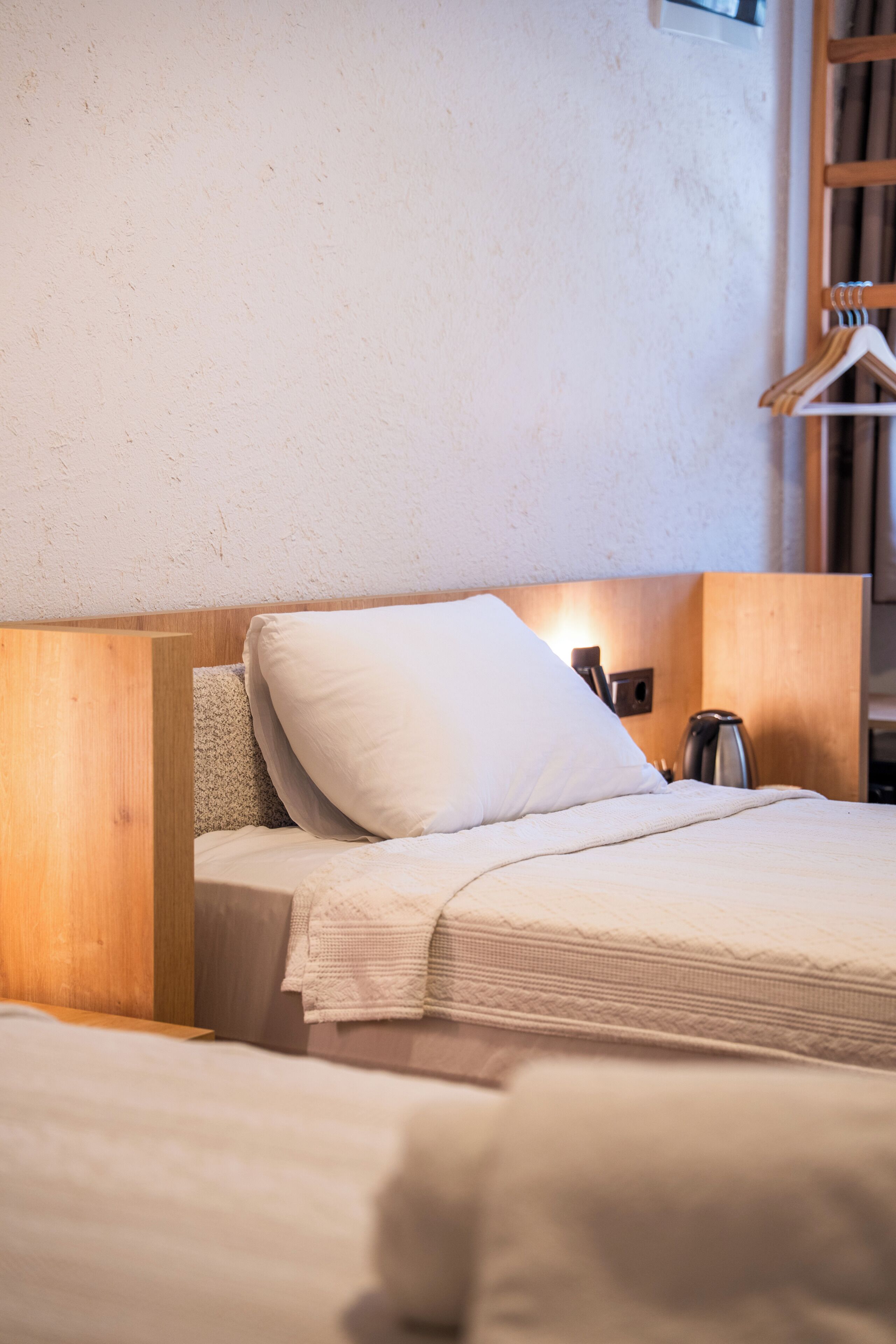 Una cama con cabecera de madera, una mesita de noche y una lámpara fijada a la pared.