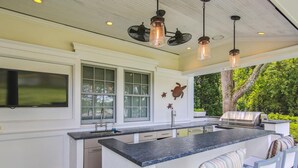Una cocina moderna con una isla grande, taburetes de bar y una parrilla afuera.