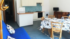A compact kitchen with a microwave, stove, and washing machine. There is a dining table with chairs and a blue sofa in the living area. - Casa Vacanze "afrodite" Centro Storico Otranto, Salento 6 Posti (Otranto)