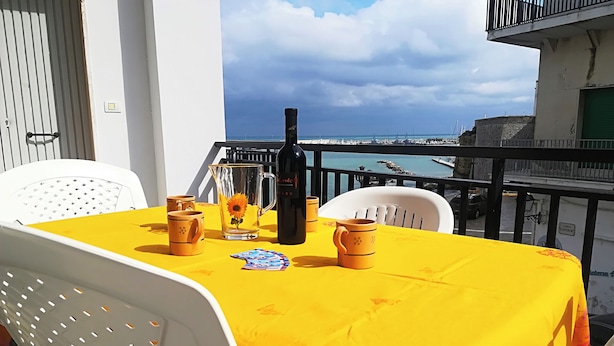A balcony with a yellow tablecloth, white chairs, a bottle, and a pitcher with a flower. - Casa Vacanze "afrodite" Centro Storico Otranto, Salento 6 Posti (Otranto)