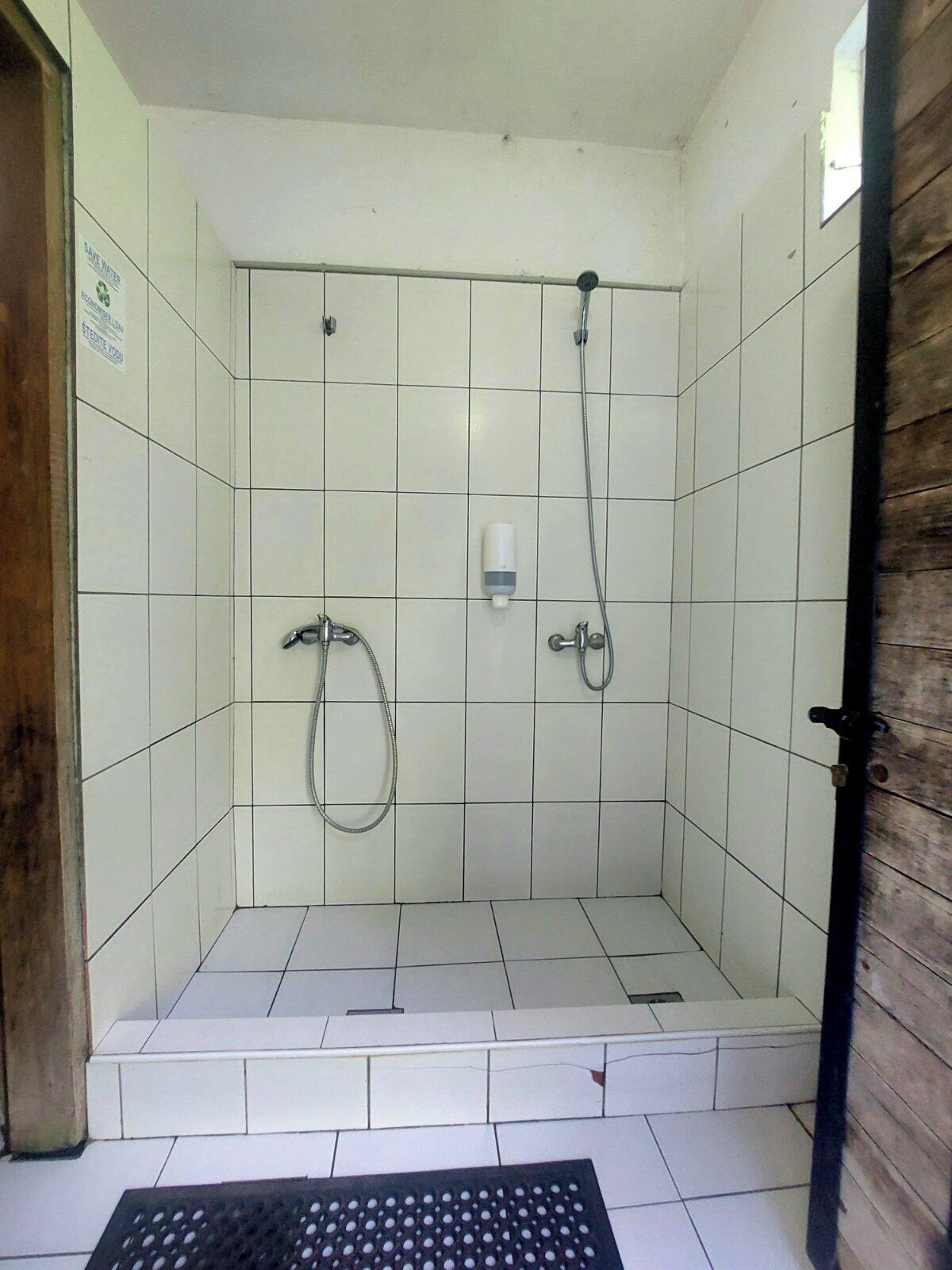 Un baño pequeño con azulejos, grifo de ducha metálico y ducha de mano.