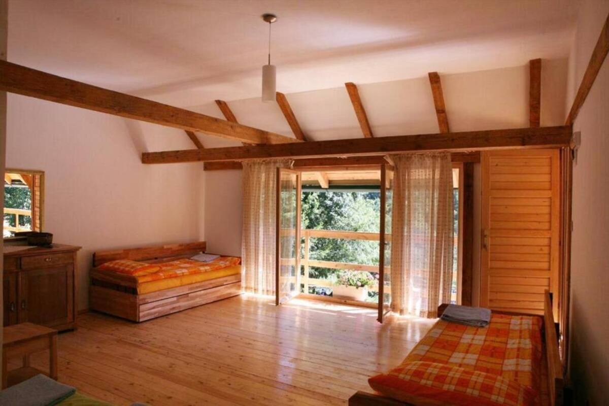 A room with wooden beams, a bed, a bench, and a view through a glass door.
