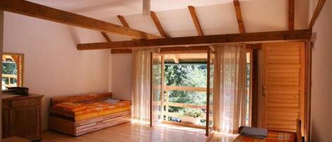 Une pièce avec des poutres en bois, un lit, un banc et une vue à travers une porte vitrée.