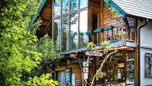 A wooden cabin with a glass front, a reception area, and a balcony with plants.