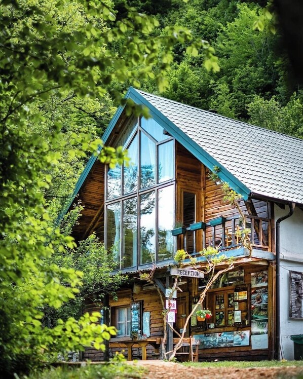 A wooden cabin with a glass front, a reception area, and a balcony with plants.