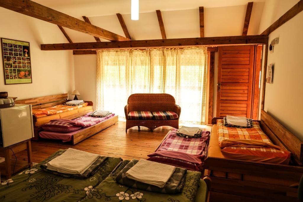 A cozy room with a bed, a chair, and a small table. There is a window with curtains, a poster on the wall, and a wooden ceiling.