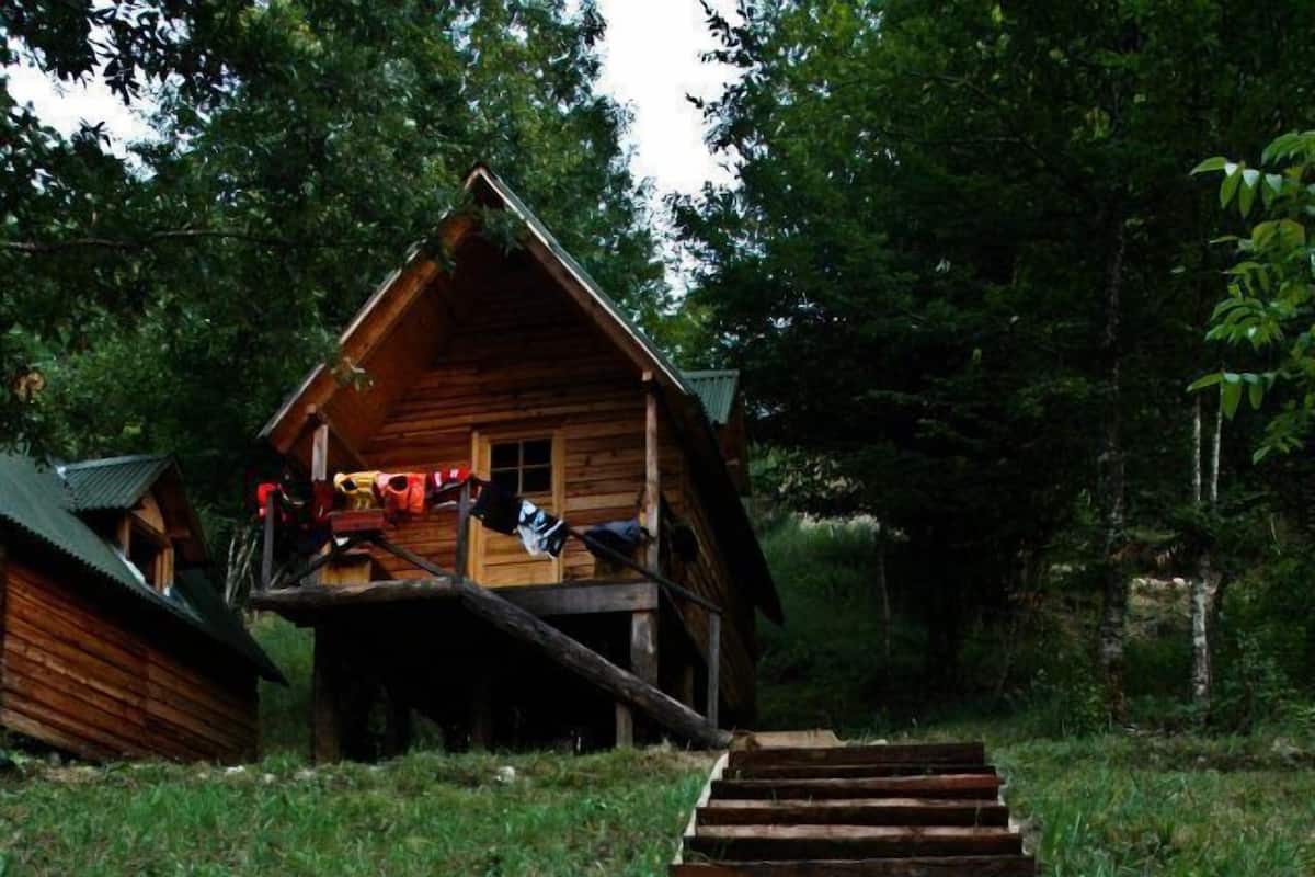 A wooden staircase leading to a cabin with a balcony, surrounded by greenery.