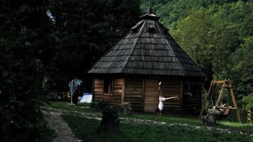 A rustic cabin with a thatched roof, surrounded by lush greenery and a stone pathway.