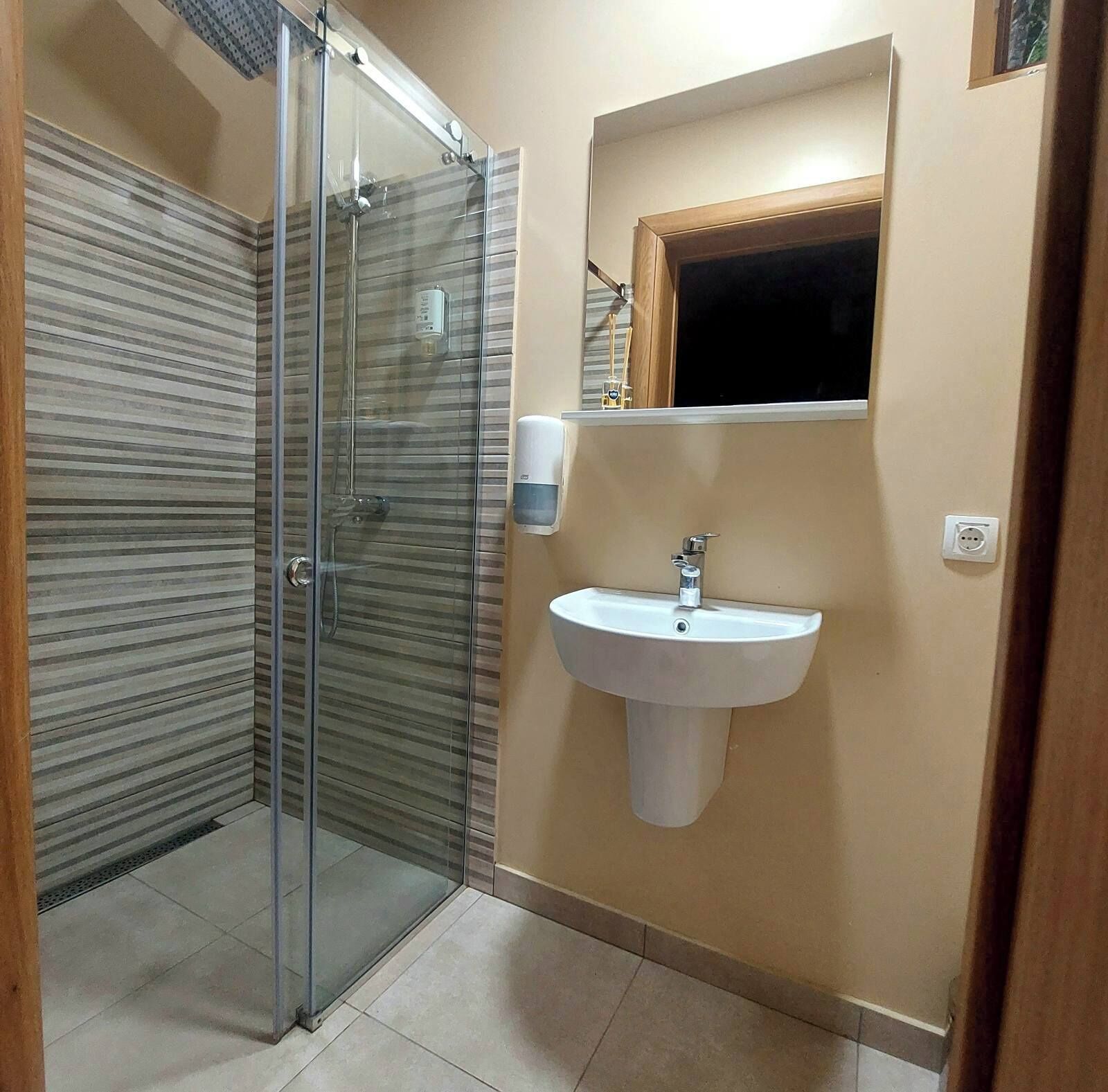 A bathroom with a glass shower enclosure, a white sink, and a mirror above it.