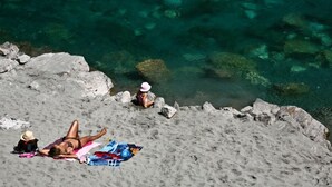 A beach with clear water, rocks, and two people relaxing.