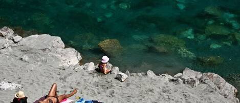 Une plage avec une eau claire, des rochers et deux personnes qui se détendent.