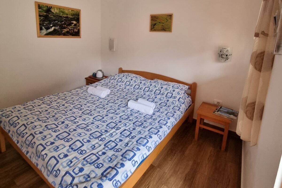 A bedroom with a wooden bed, a bedside table, a nightstand, a hanging light fixture, and two framed pictures on the wall.