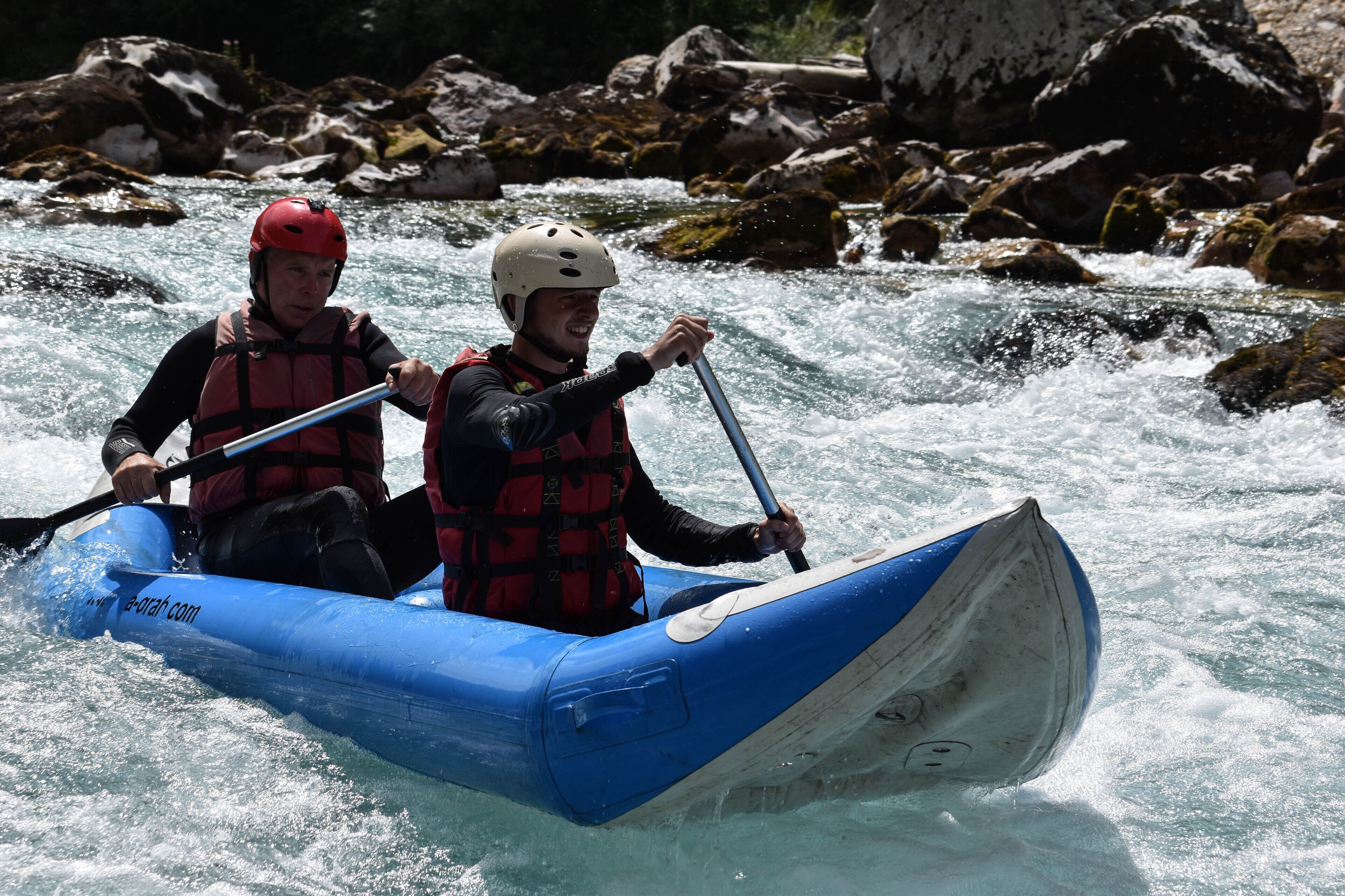 Two people in a blue inflatable raft navigating a river with rapids.