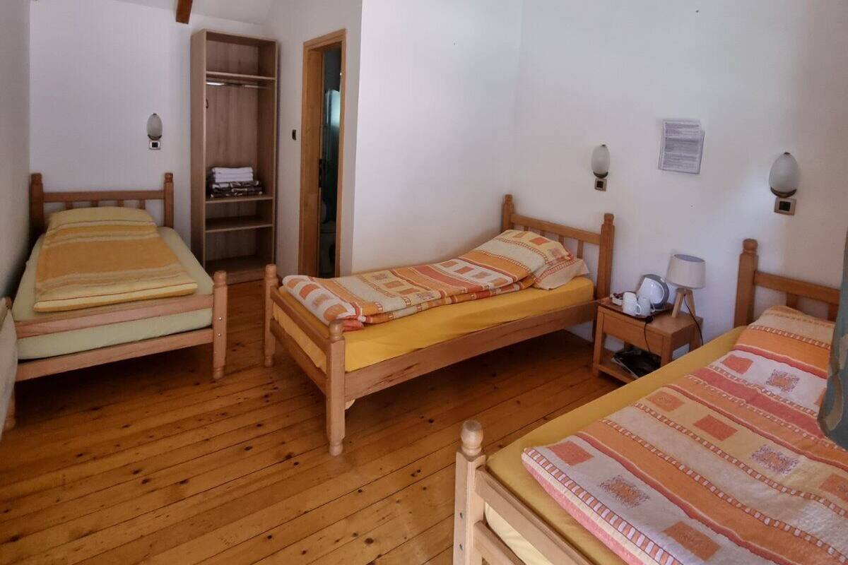 A room with two wooden beds, a wooden wardrobe, and a small table with a lamp.