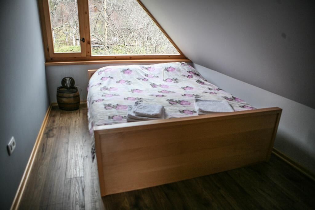 Una habitación pequeña con cama individual, techo inclinado y ventana con vistas a un área boscosa.