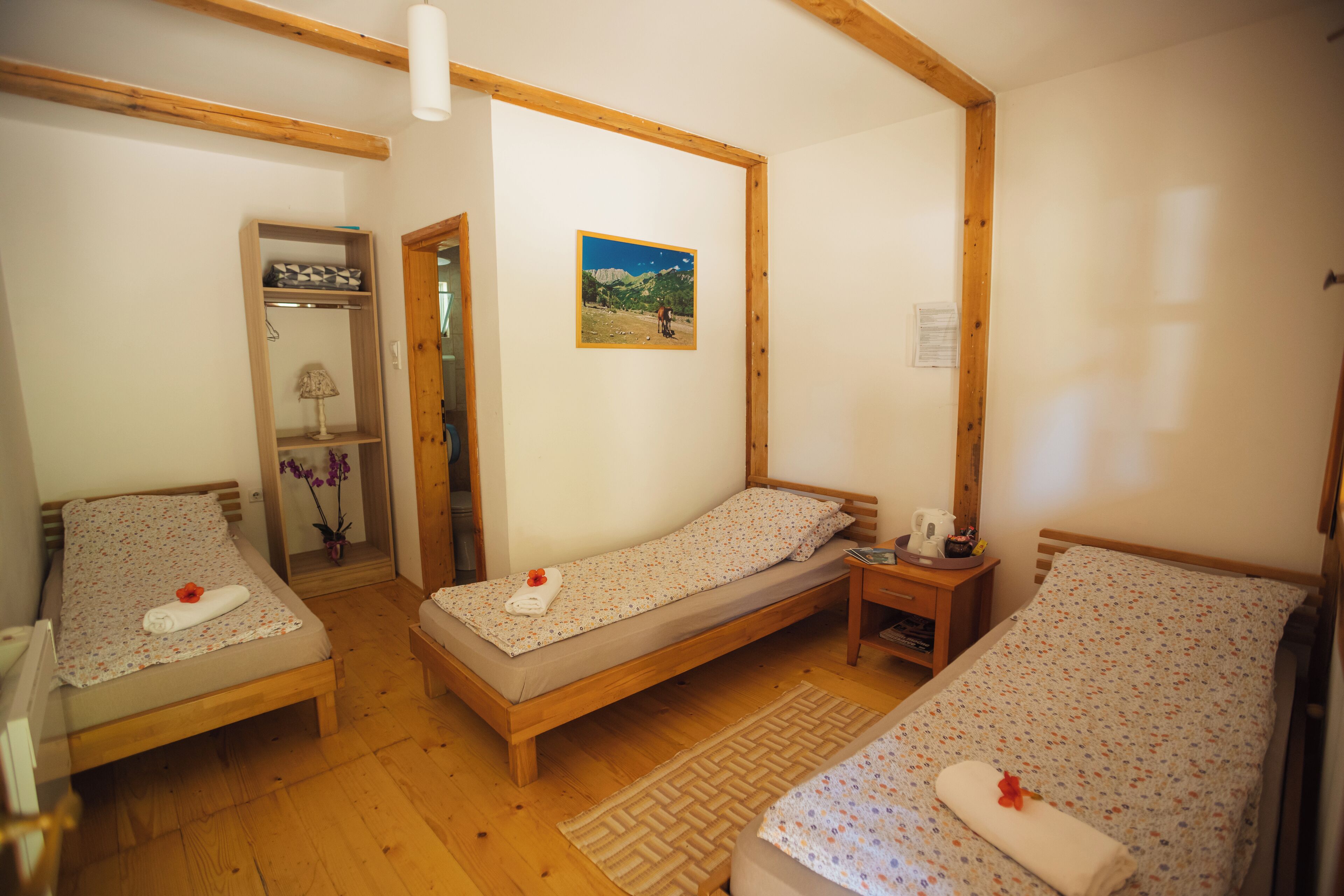 A room with three wooden beds, a wooden wardrobe, a mirror, and a framed picture on the wall.