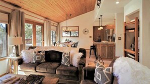 Uma sala de estar aconchegante com um sofá marrom escuro, uma área de jantar com mesa de madeira e uma cozinha com armários de madeira e eletrodomésticos de aço inoxidável.