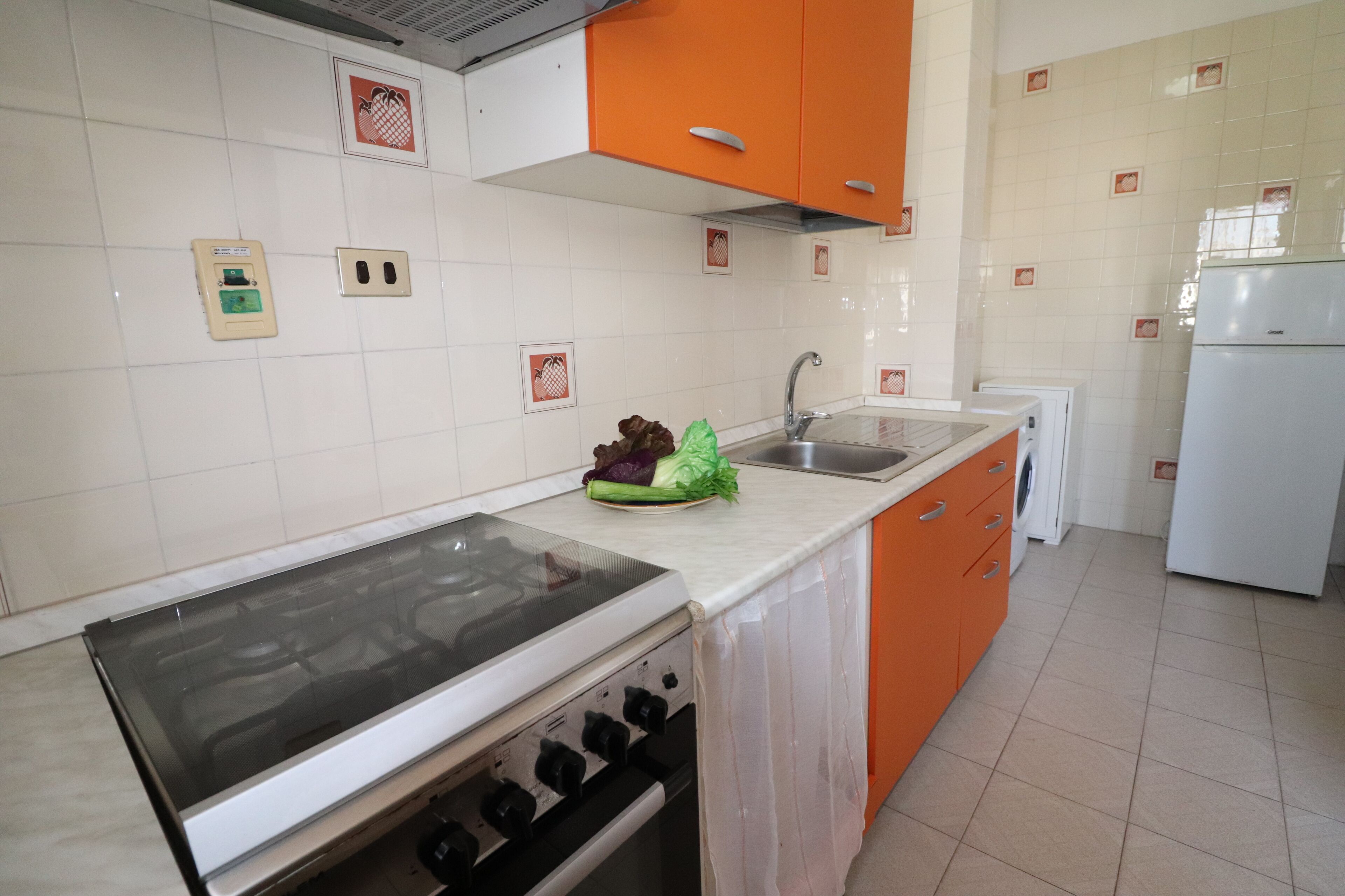 Eine Küche mit weißen und orangefarbenen Schränken, einem Herd, einem Spülbecken und einem Kühlschrank.