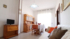 Una habitación con una cama, un televisor sobre un mueble de madera, una mesa de comedor con sillas y una zona de cocina.