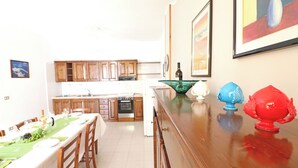 A kitchen with wooden cabinets, a dining table set for four, and a kitchen island with a green bowl. - Casa Vacanze Rita 1 Comfort and Space Just Steps From the Sea in Beautiful Otr (Otranto)