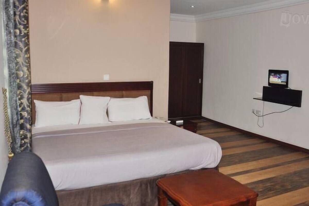 Habitación de hotel con una cama grande, una mesita pequeña, un televisor montado en la pared y un armario.