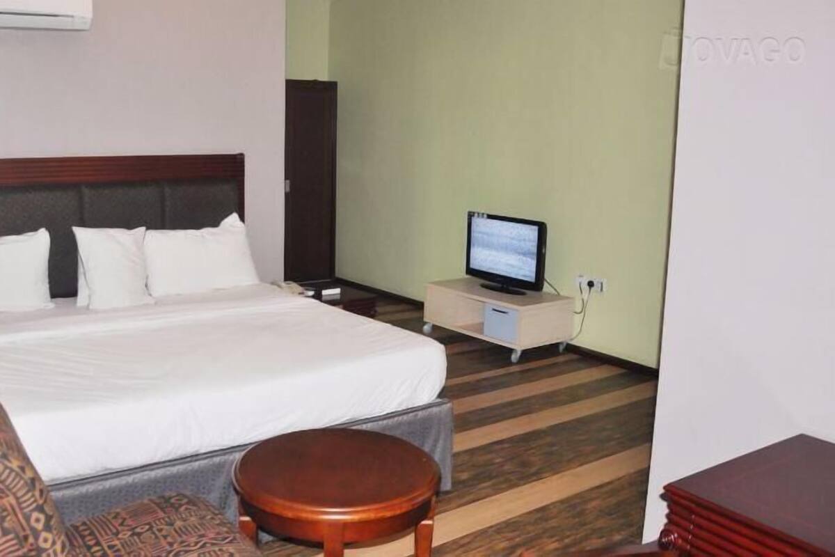 Una habitación de hotel con una cama, un televisor sobre un soporte, una silla y una mesita.