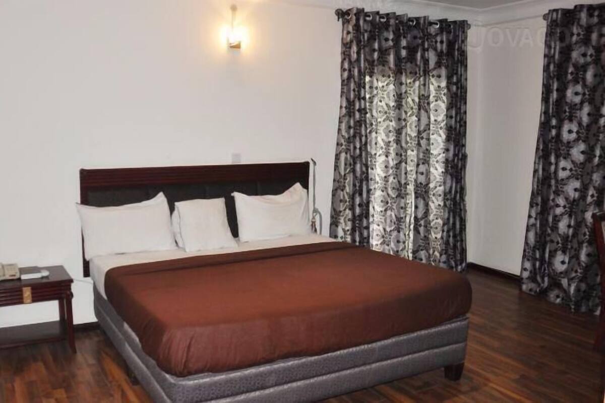 Un dormitorio con cama de madera, almohadas blancas, una mesita de noche y cortinas estampadas.