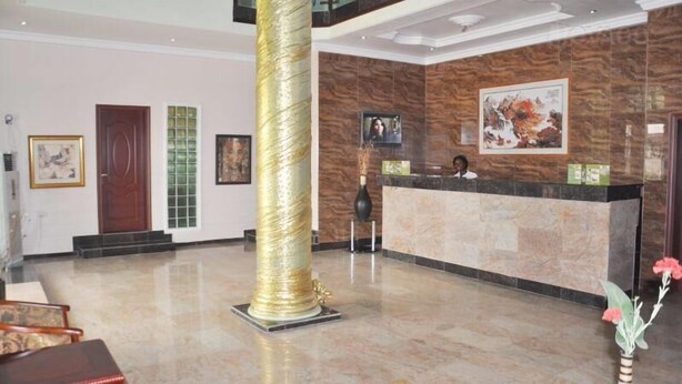 A reception area with a marble floor, a receptionist desk, a large gold pillar, and framed artwork on the walls. - Denami Suites (Port Harcourt)