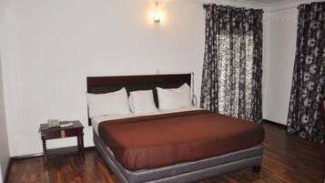 A bedroom with a wooden bed, white pillows, a nightstand, and a patterned curtain.