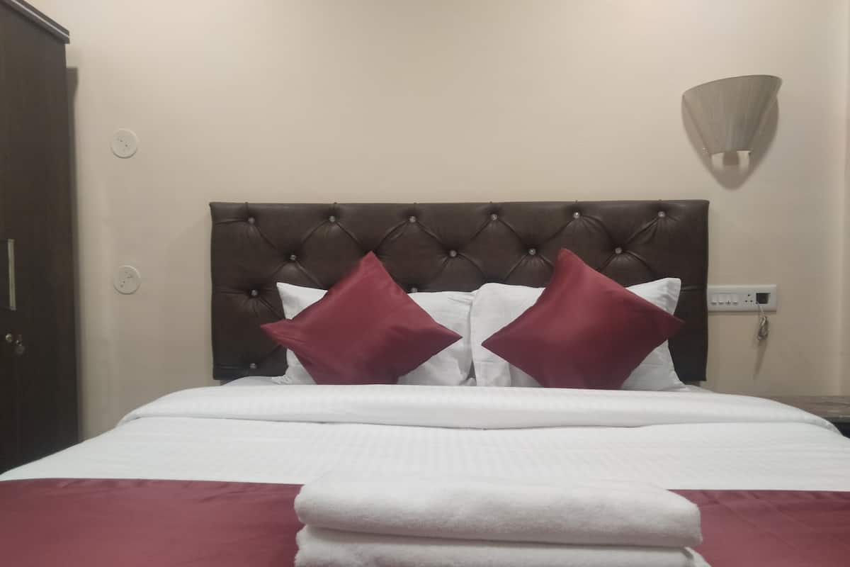 A neatly made bed with a tufted headboard, two red pillows, and folded white towels on a red bedspread.