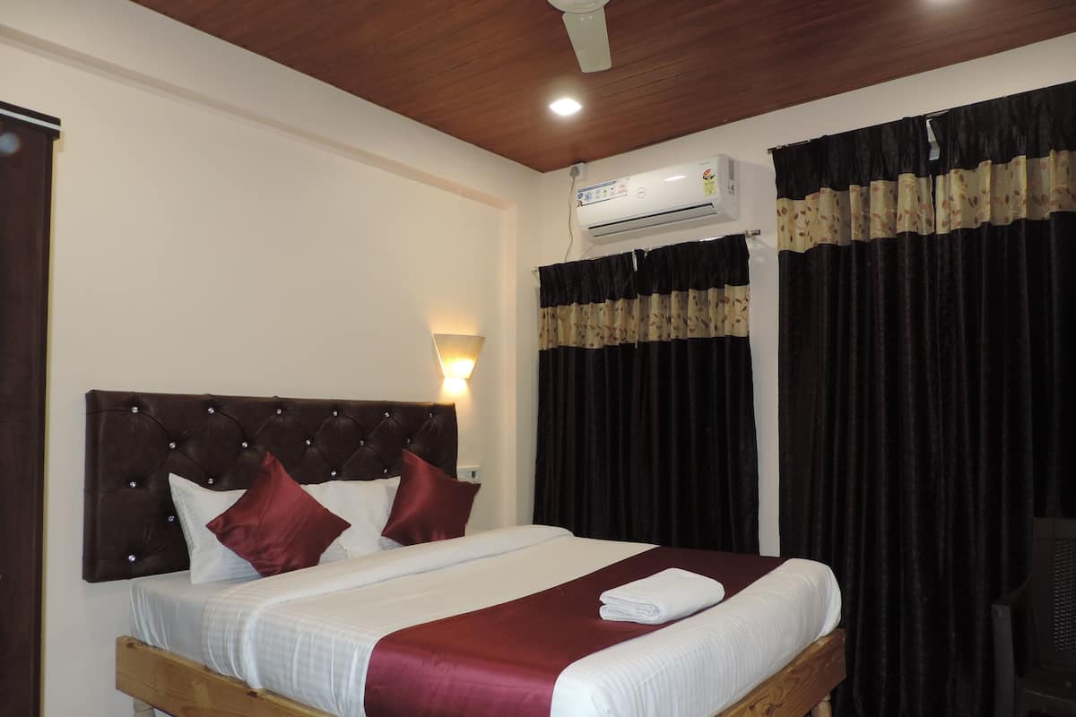 A hotel room with a wooden bed, a wall-mounted air conditioner, a wall lamp, and a window with dark curtains.