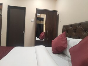 A hotel room with a bed, a mirror, a wardrobe, and a door. - Punest Hospitality & Hotel (Pune)