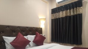 A neatly made bed with white and maroon bedding, a tufted headboard, and a wall-mounted light fixture. - Punest Hospitality & Hotel (Pune)