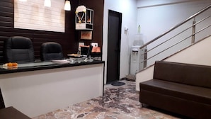 A reception area with a marble floor, two black chairs, a counter with a glass top, and a staircase with a metal railing. - Punest Hospitality & Hotel (Pune)
