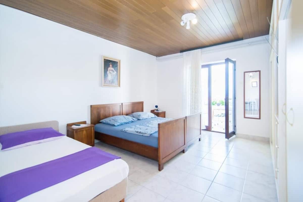 A bedroom with a wooden ceiling, a bed with a blue and white bedspread, a nightstand, and a painting on the wall.