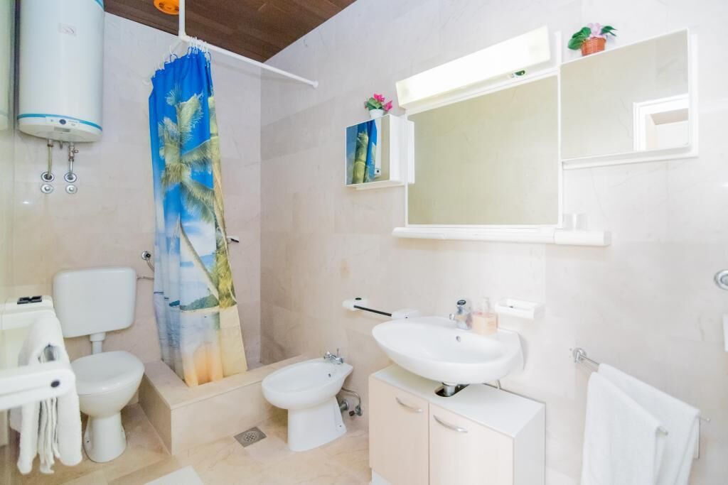 A bathroom with a shower curtain, a sink, a toilet, a bidet, and a towel rack.