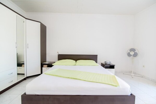 Un dormitorio con cama, mesitas de noche, espejo y un ventilador de pie.