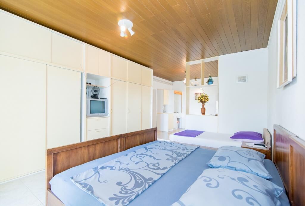 A bedroom with a wooden ceiling, a bed with patterned bedding, a TV, and a mirror.