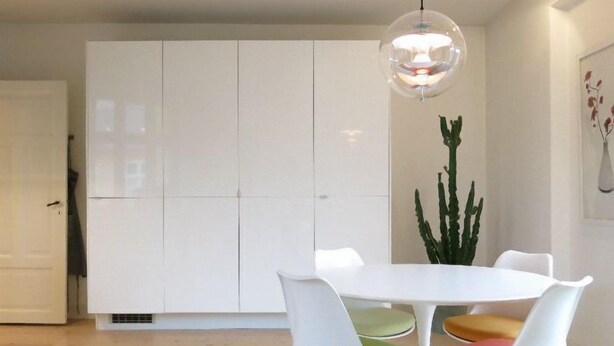 Un espace repas moderne avec une table et des chaises blanches, un luminaire suspendu et une grande plante.