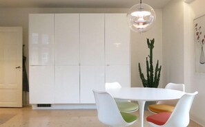 A modern dining area with a white table and chairs, a hanging light fixture, and a tall plant. - Apartment Peder Skrams Gade 664-1 (Copenhagen)