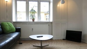 Un salon avec un canapé en cuir noir, une petite table blanche, une plante en pot et un radiateur.
