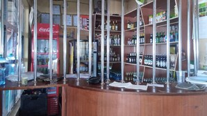 A bar area with shelves stocked with various beverages, a Coca-Cola refrigerator, and a counter with a cash register.