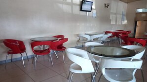 A dining area with red and white chairs and tables, a flat-screen TV on the wall, and a tiled floor.