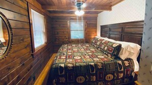 Un dormitorio acogedor con techo de madera, colcha acolchada y ventana con persianas.