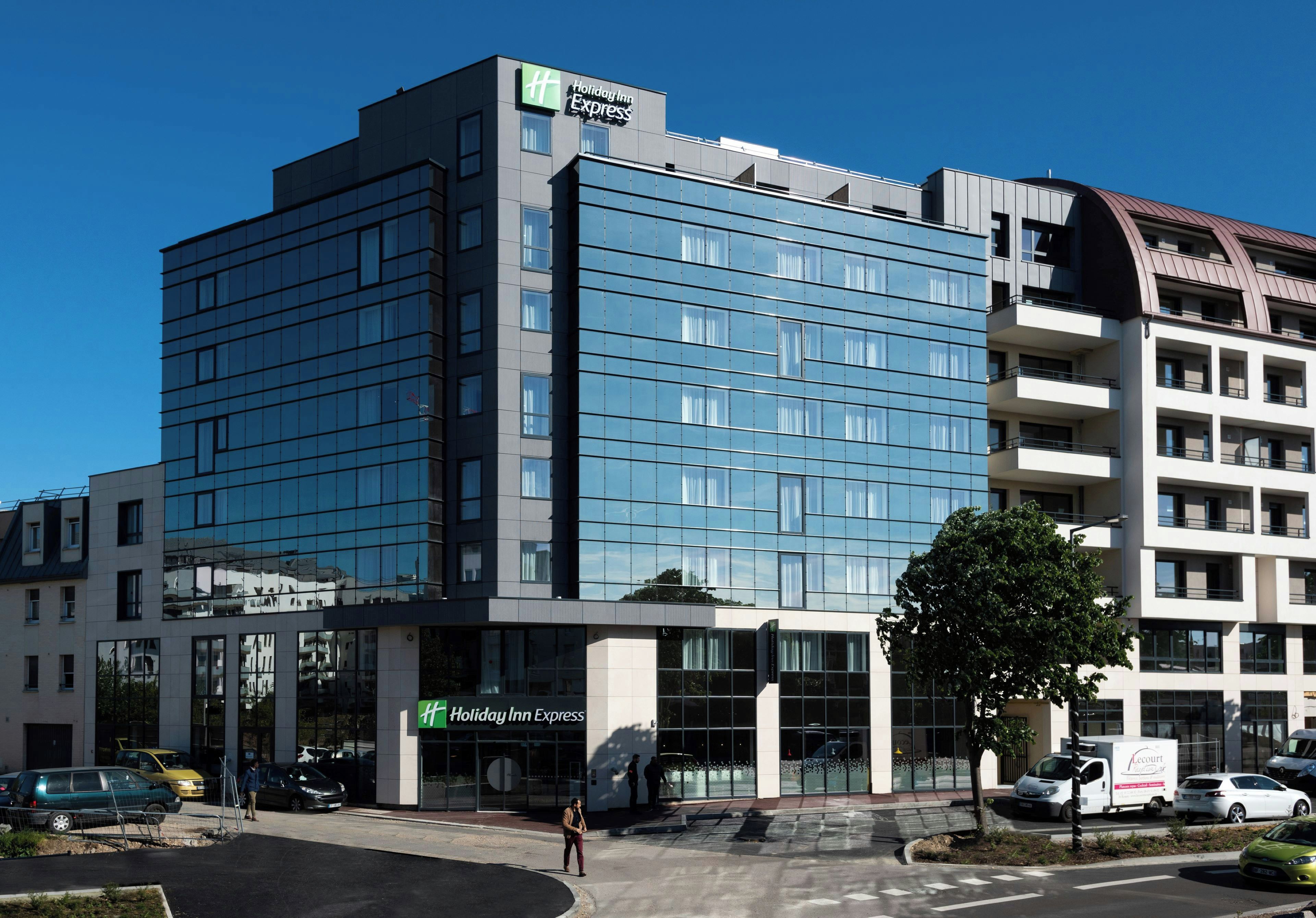 Un edificio de hotel moderno con el letrero de Holiday Inn Express, amplias ventanas y un estacionamiento con automóviles.