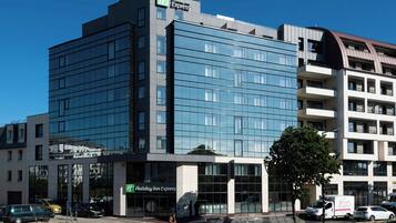 Un edificio de hotel moderno con el letrero de Holiday Inn Express, amplias ventanas y un estacionamiento con automóviles.