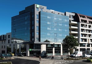 A modern hotel building with a Holiday Inn Express sign, large windows, and a parking area with cars. - Holiday Inn Express Rouen Centre-rive Gauche (Rouen)