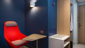 A modern hotel room with a red chair, a small table, and a wooden wardrobe.