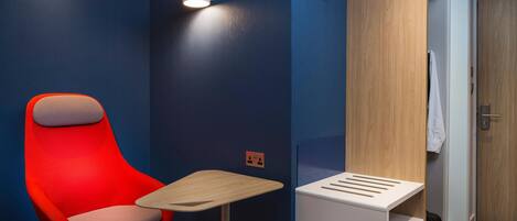 Una habitación de hotel moderna con una silla roja, una mesita pequeña y un armario de madera.
