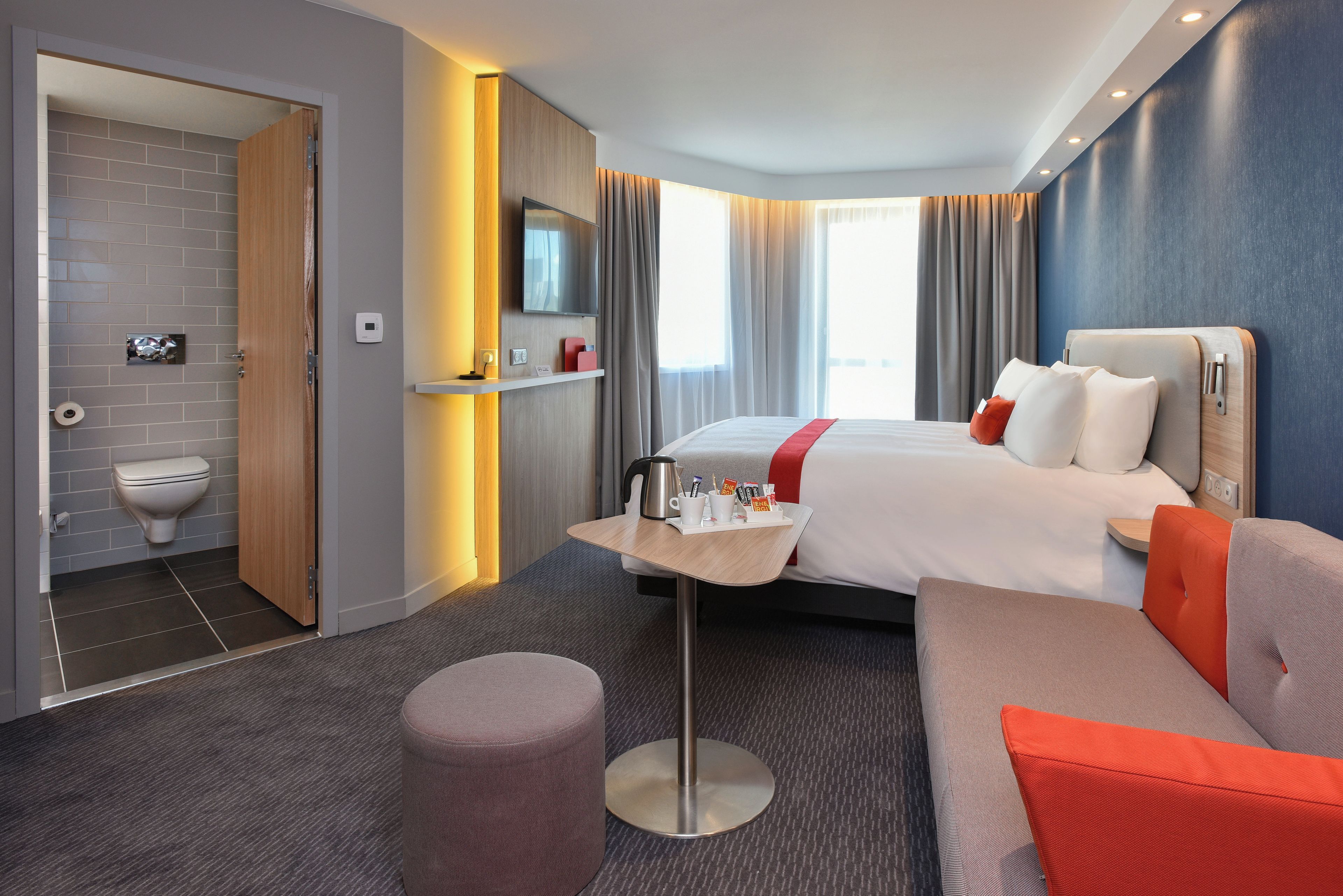 Habitación de hotel con cama, sofá, una mesita con artículos de aseo, inodoro y zona de ducha.
